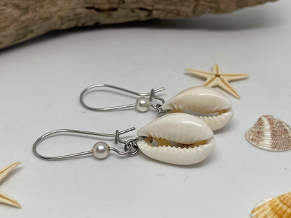 Shell earrings with silver hooks on a white surface with starfish and shells.