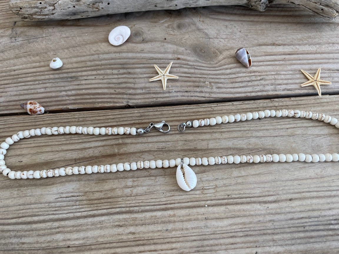 Necklace with shell beads on a wooden surface with shells and starfish.