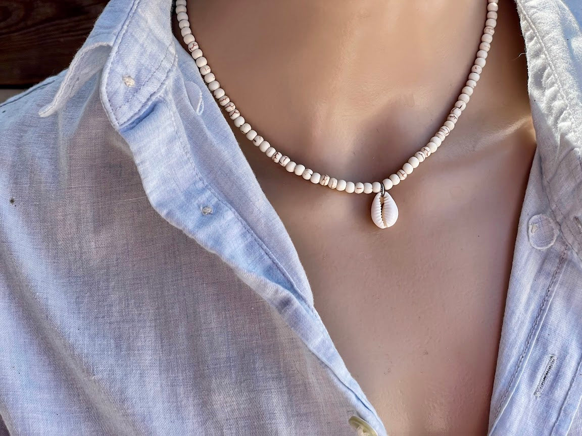 Necklace with a shell pendant worn by a person in a light blue shirt.