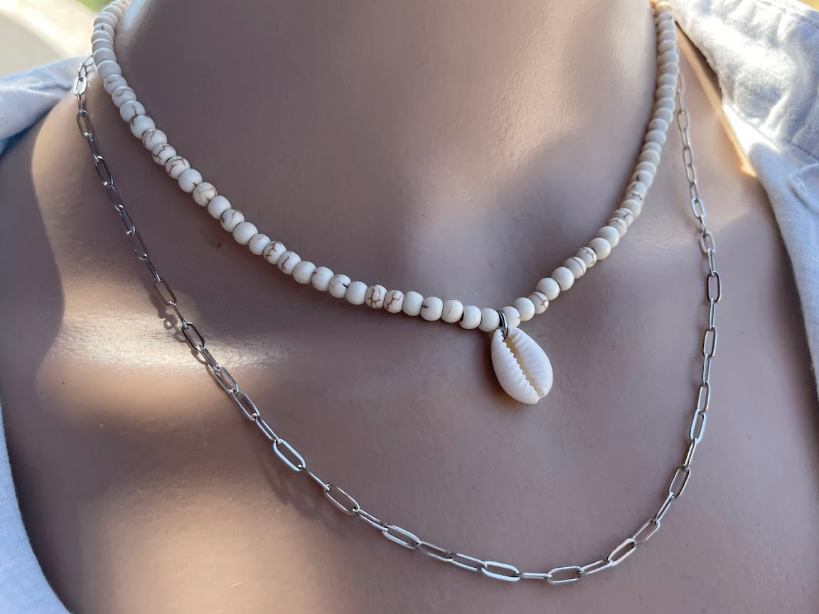 Necklace with white beads and a shell pendant on a mannequin.