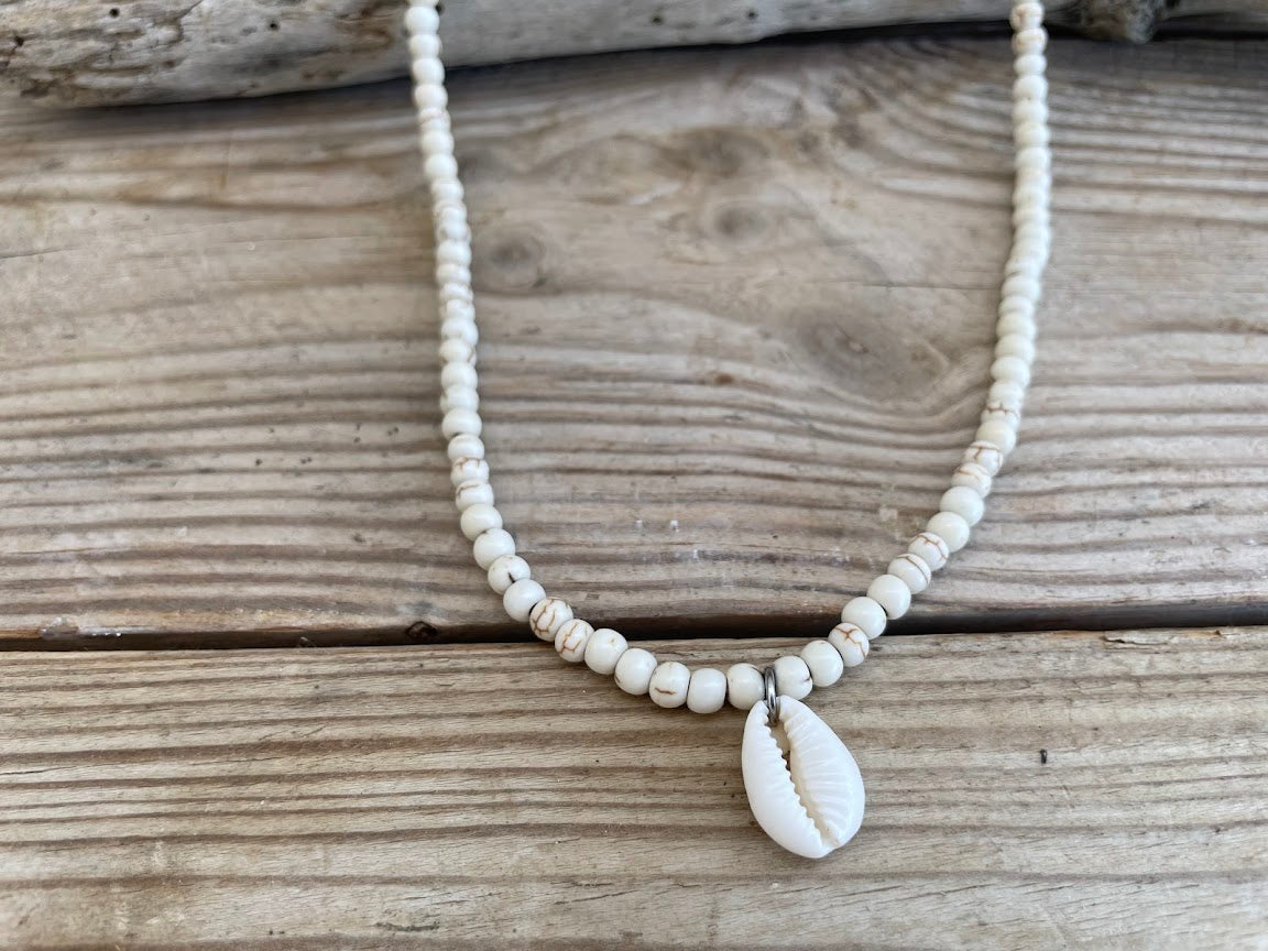 Necklace with white beads and a shell pendant on a wooden surface