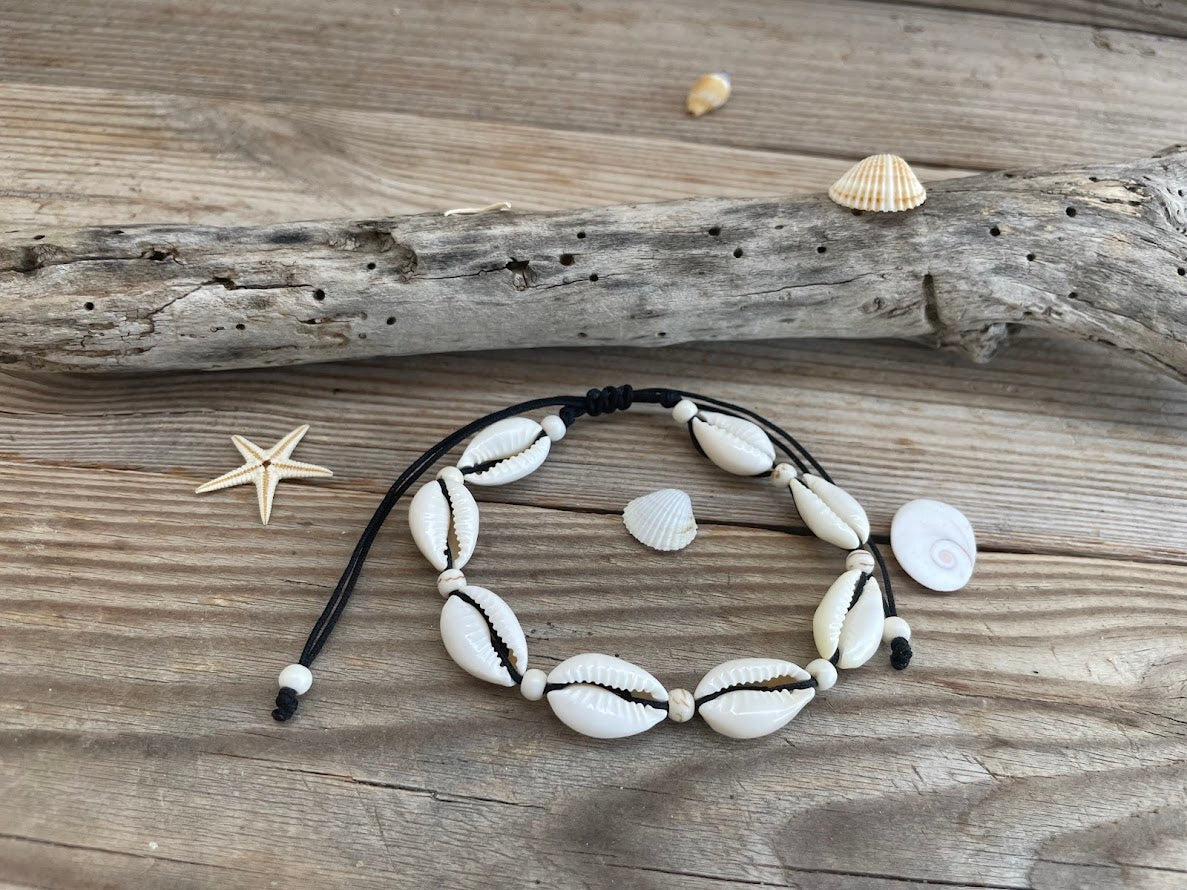 Bracelet with cowrie shell beads on a wooden surface with shells and a starfish.