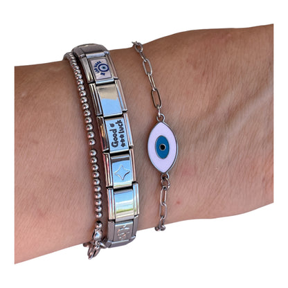 Wrist wearing a silver bracelet with a blue eye design and another bracelet with text on a white background