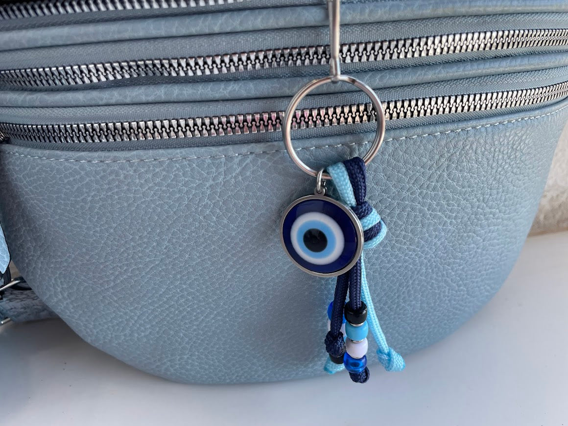 Blue evil eye keychain hanging from a gray bag
