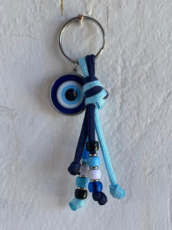 Keychain with blue and white beads and an evil eye charm on a light gray background