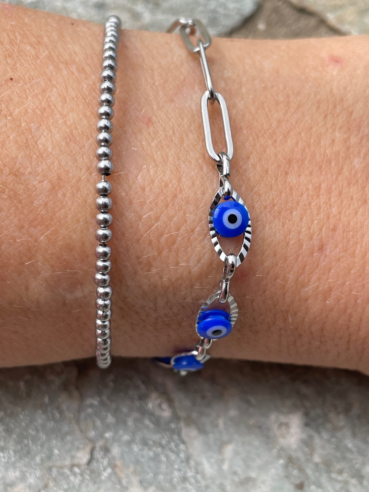 Silver bracelet with blue evil eye charms on a wrist against a neutral background