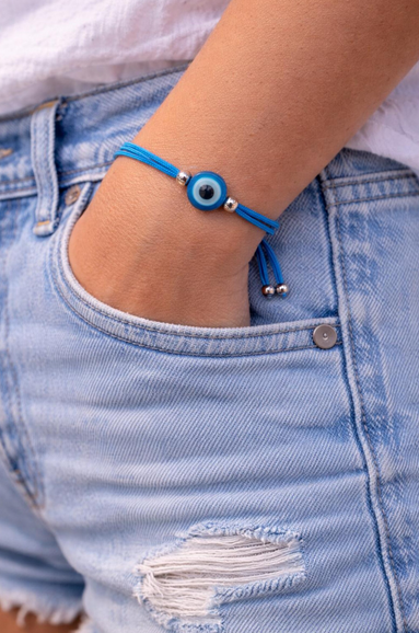 Blue bracelet with a silver bead on a wrist, wearing light blue denim shorts.