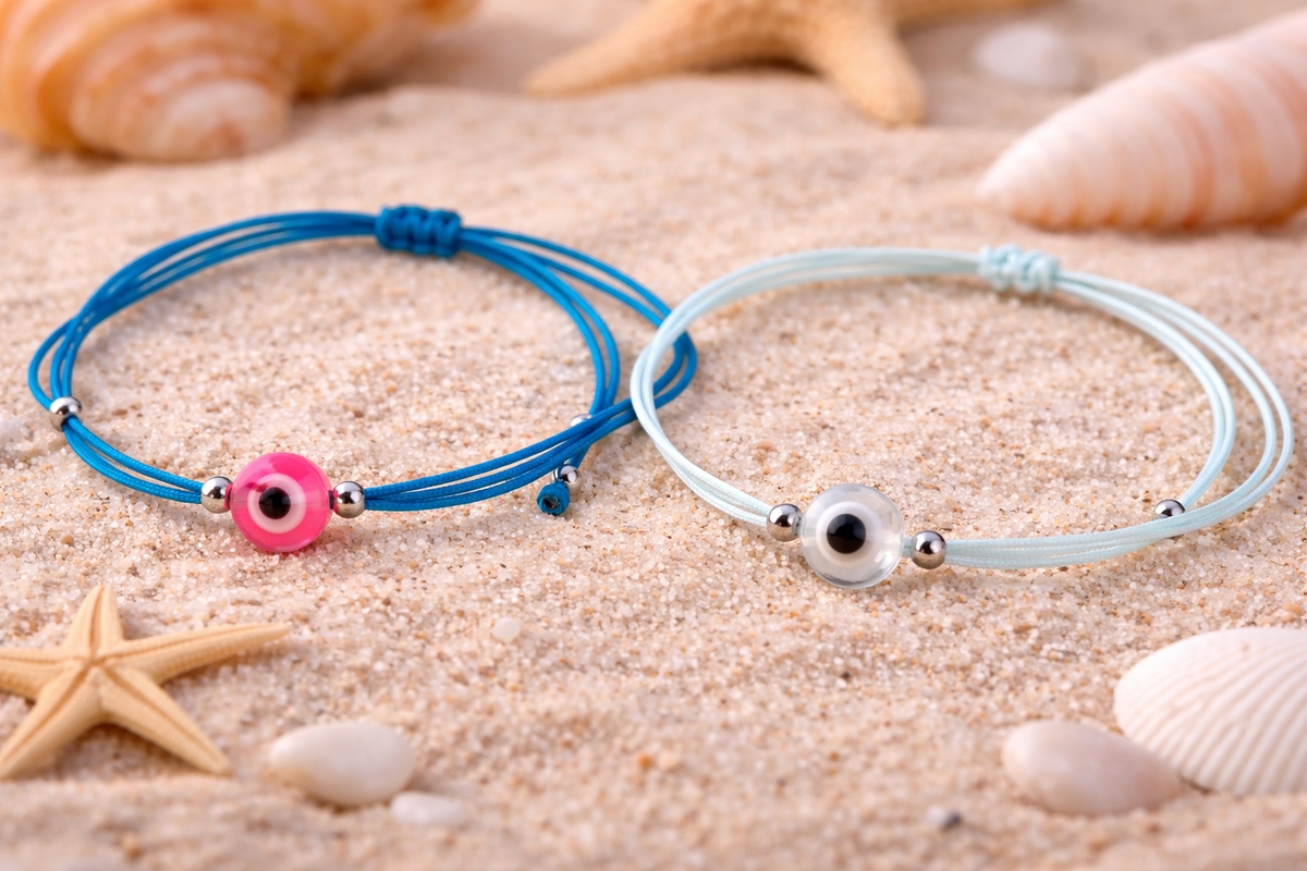 Two bracelets, one blue and one white, on sand with starfish and shells.