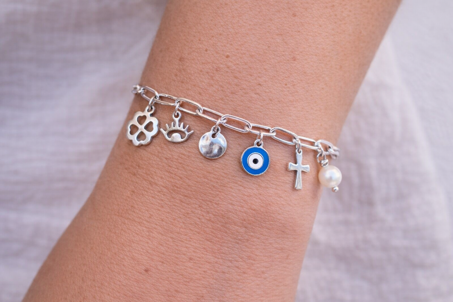 Silver bracelet with various charms on a wrist against a neutral background