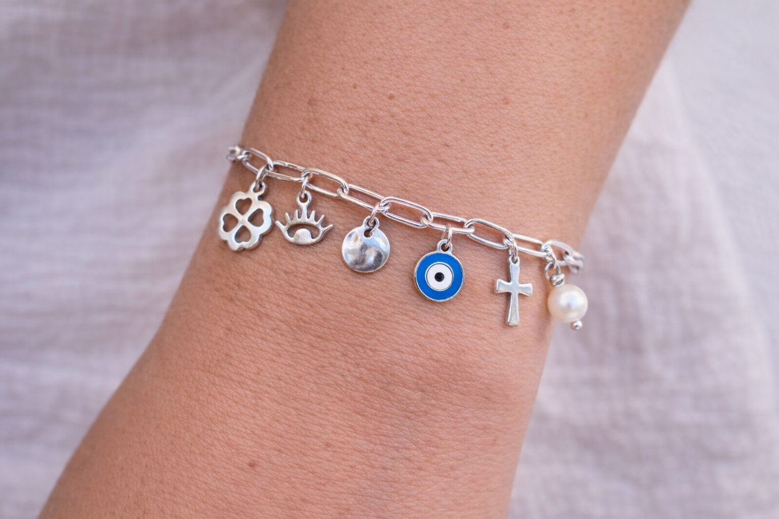 Silver bracelet with various charms on a wrist against a neutral background