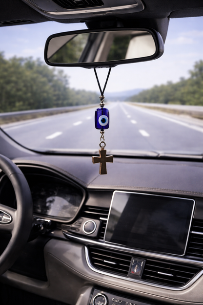 Car interior with a hanging amulet featuring a blue eye and cross on a road.