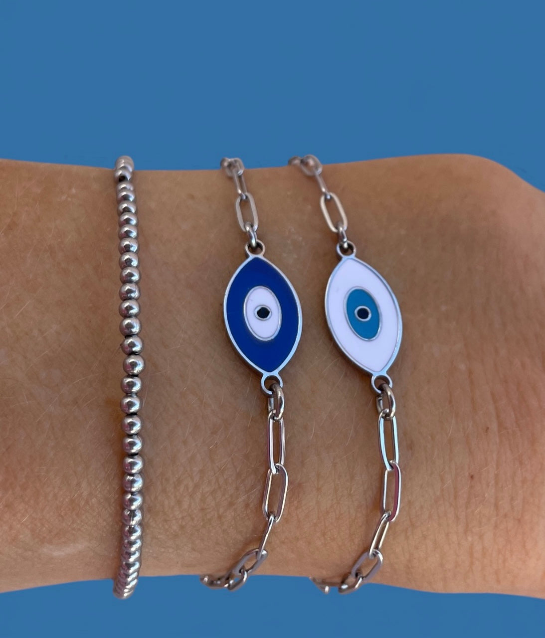 Two silver bracelets with blue and white eye designs on a wrist against a blue background