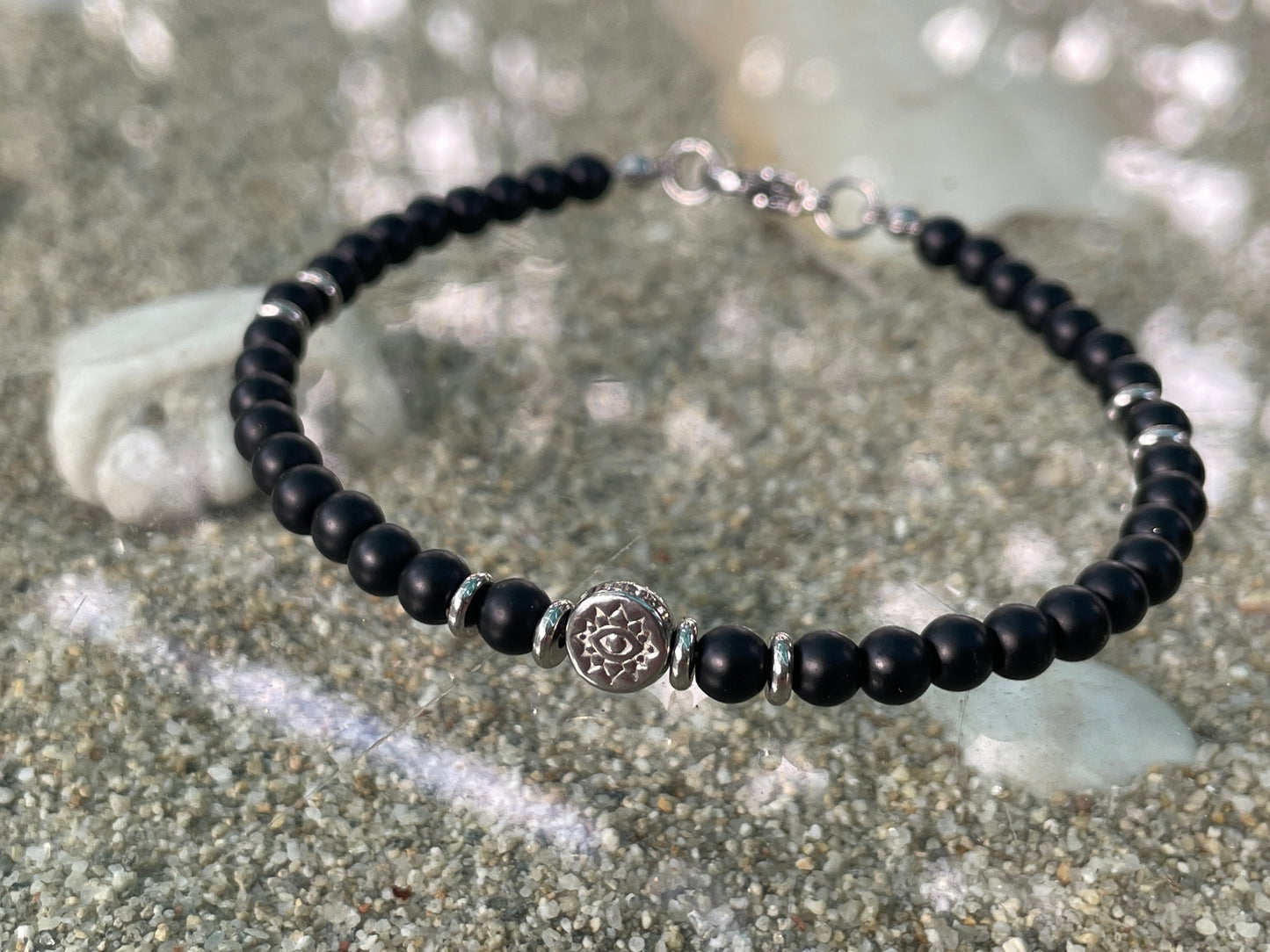 Black beaded bracelet with a silver charm on a sandy surface