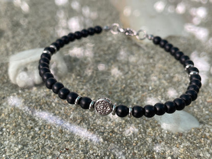 Black beaded bracelet with a silver charm on a sandy surface