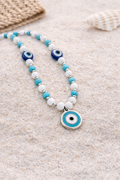 Necklace with blue and white evil eye charms on a sandy background