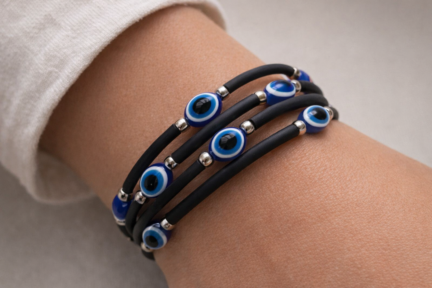 Black rubber bracelet with blue evil eye beads on a wrist against a neutral background