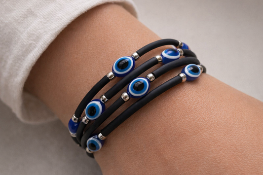 Black rubber bracelet with blue evil eye beads on a wrist against a neutral background
