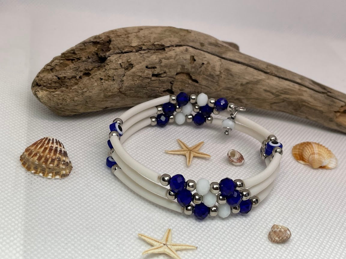 White bracelet with blue and silver beads on a white surface with driftwood and shells.