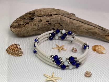 White bracelet with blue and silver beads on a white surface with driftwood and shells.
