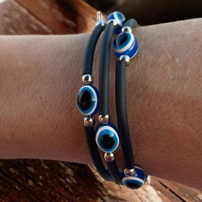 Black bracelets with blue and silver evil eye beads on a wrist.