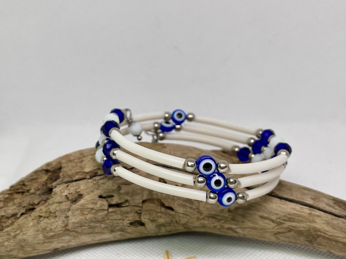 white bracelets with blue and silver evil eye beads on a wooden surface.