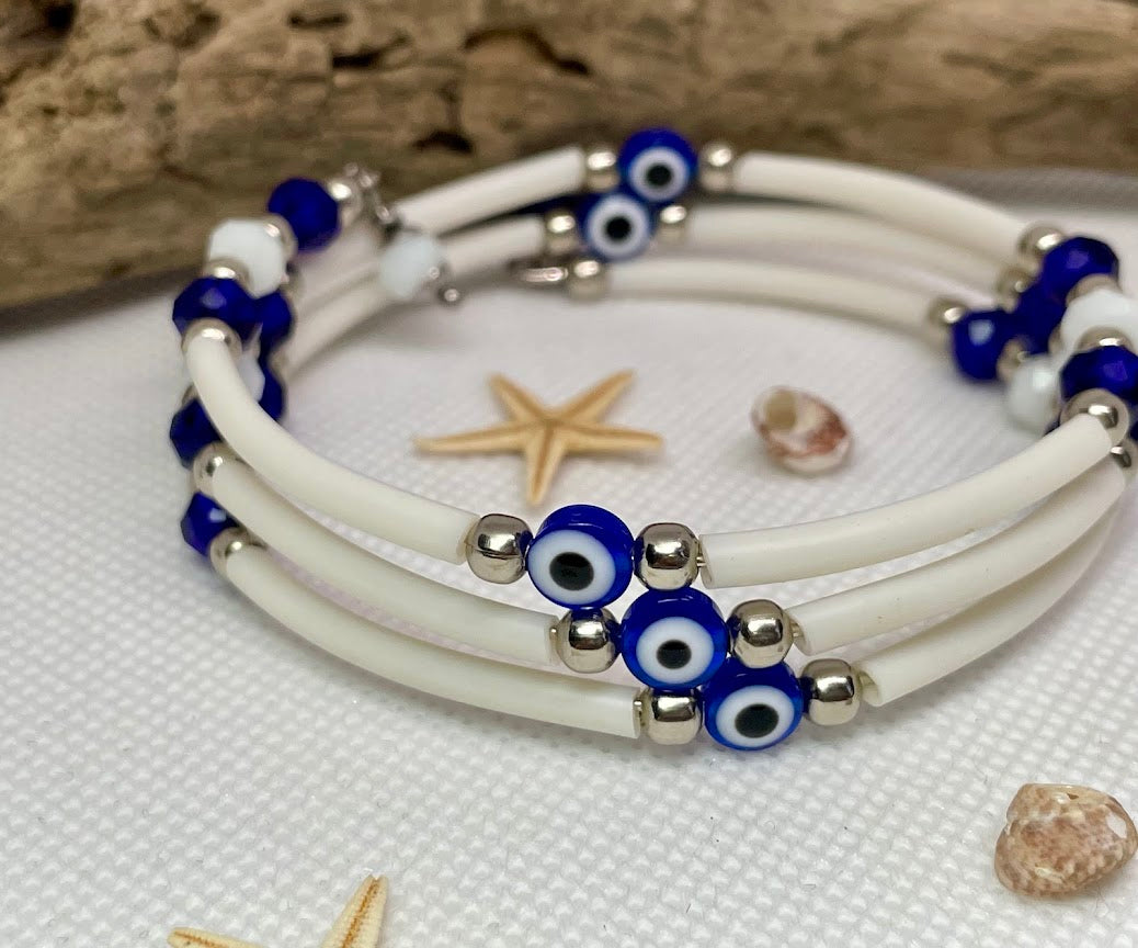 White rubber bracelet with blue and silver beads on a textured surface with starfish and shells.