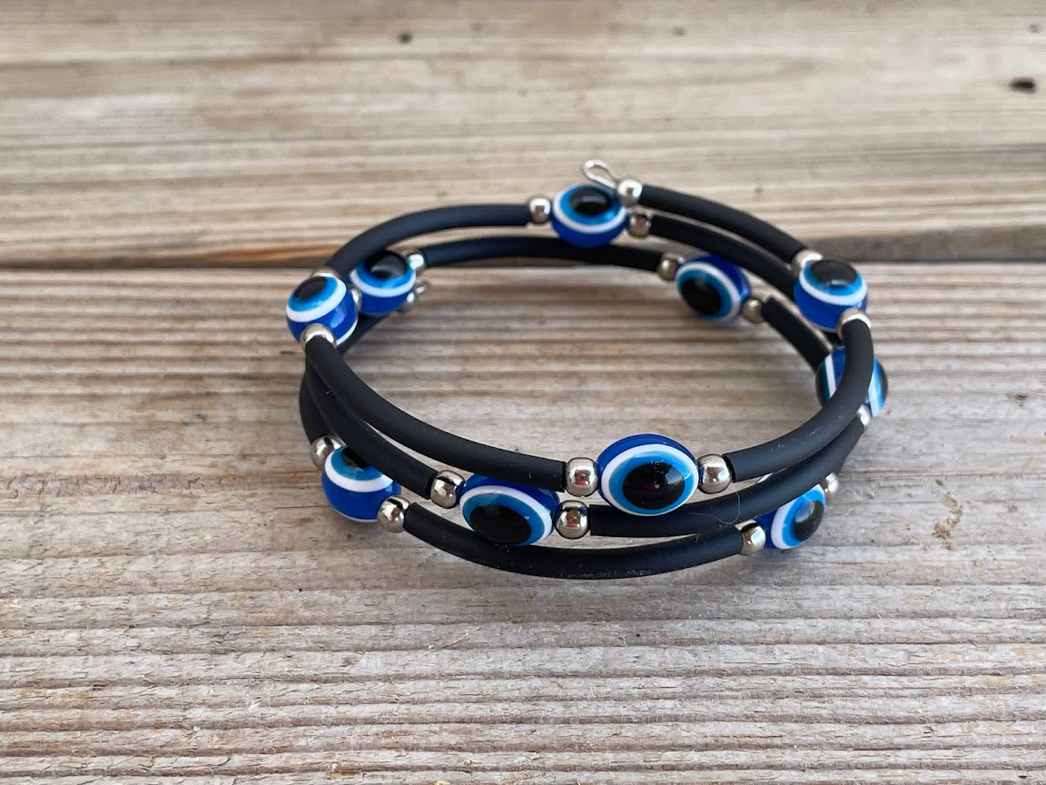 Black rubber bracelet with blue evil eye charms on a wooden surface
