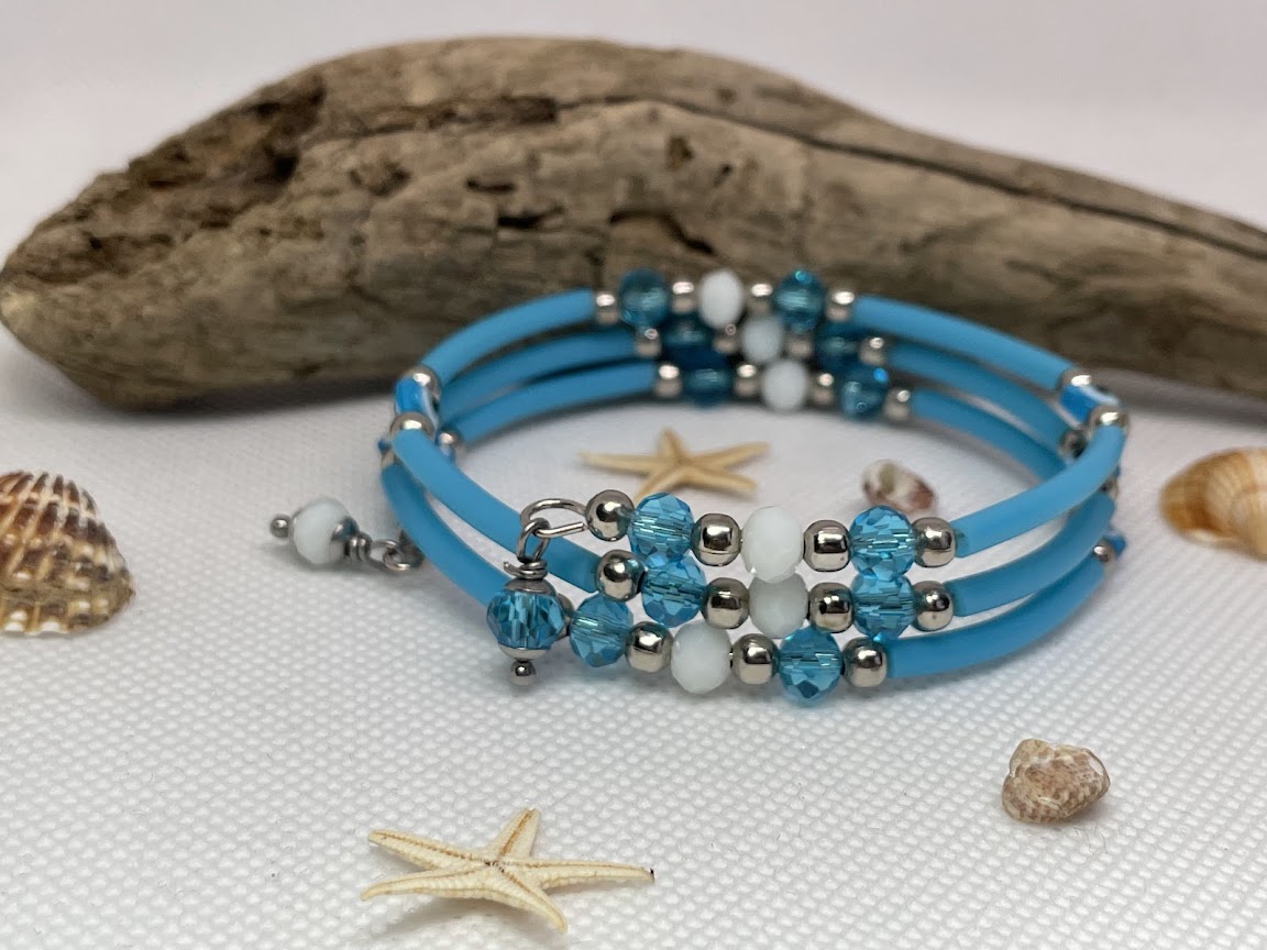 Blue beaded bracelet with silver and white beads on a textured surface with shells and starfish.