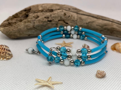 Blue beaded bracelet with silver and white beads on a textured surface with shells and starfish.