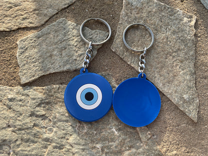 Two blue evil eye keychains on a stone surface front and back