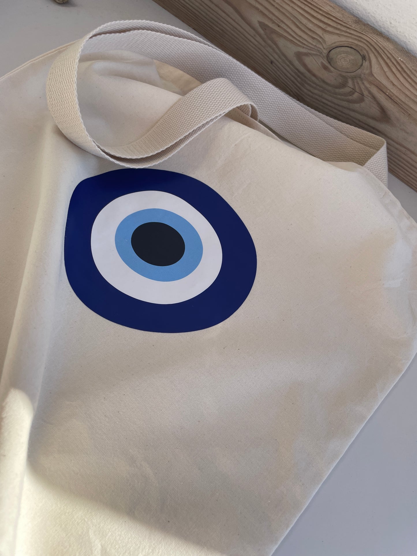 Beige tote bag with a blue and white circular design on a wooden surface.