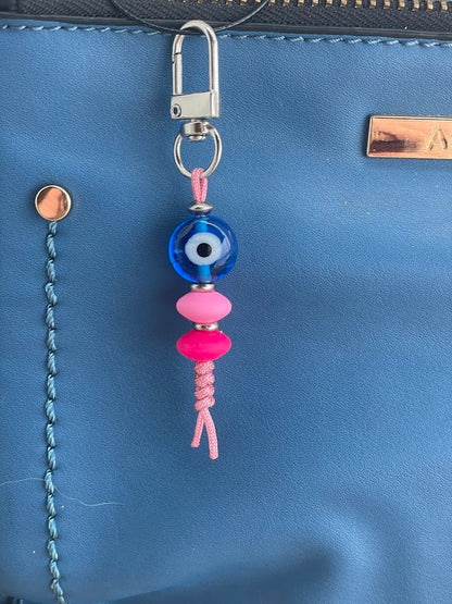 A blue glass evil eye bag charm with a silver tone snap clasp, displayed in front of a brown handbag.