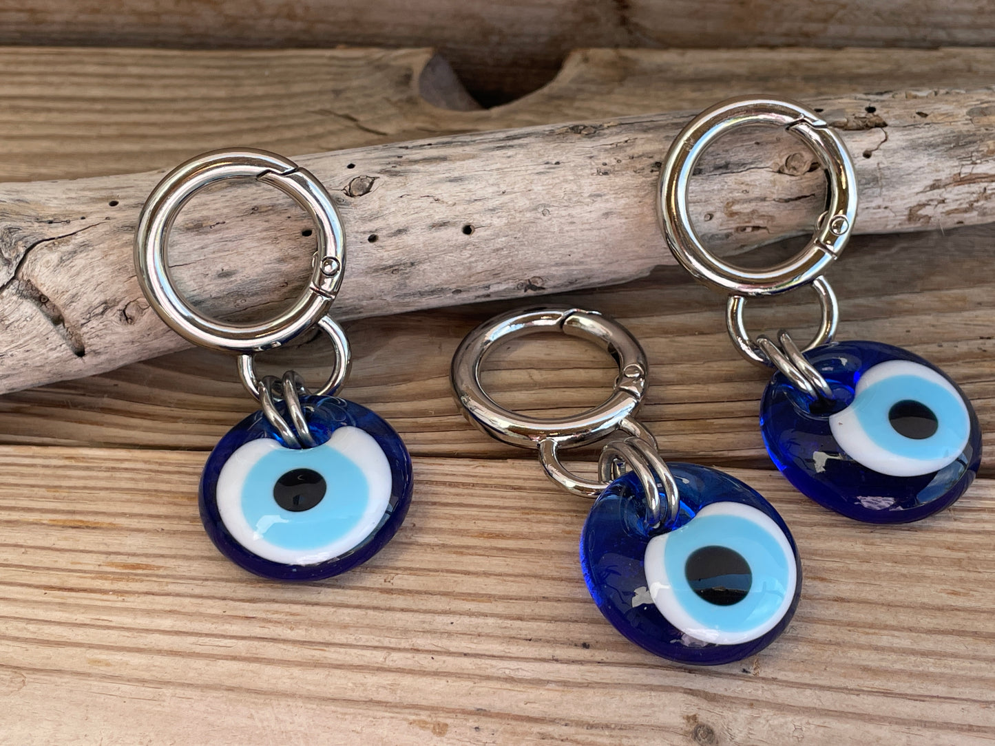 Three blue evil eye charms on silver rings placed on wooden driftwood.