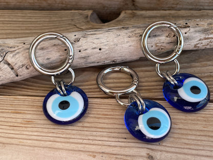 Three blue evil eye charms on silver rings placed on wooden driftwood.