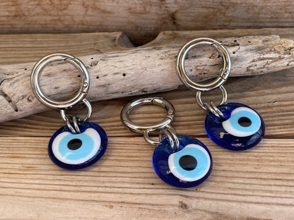 Three blue evil eye charms on silver rings placed on wooden driftwood.
