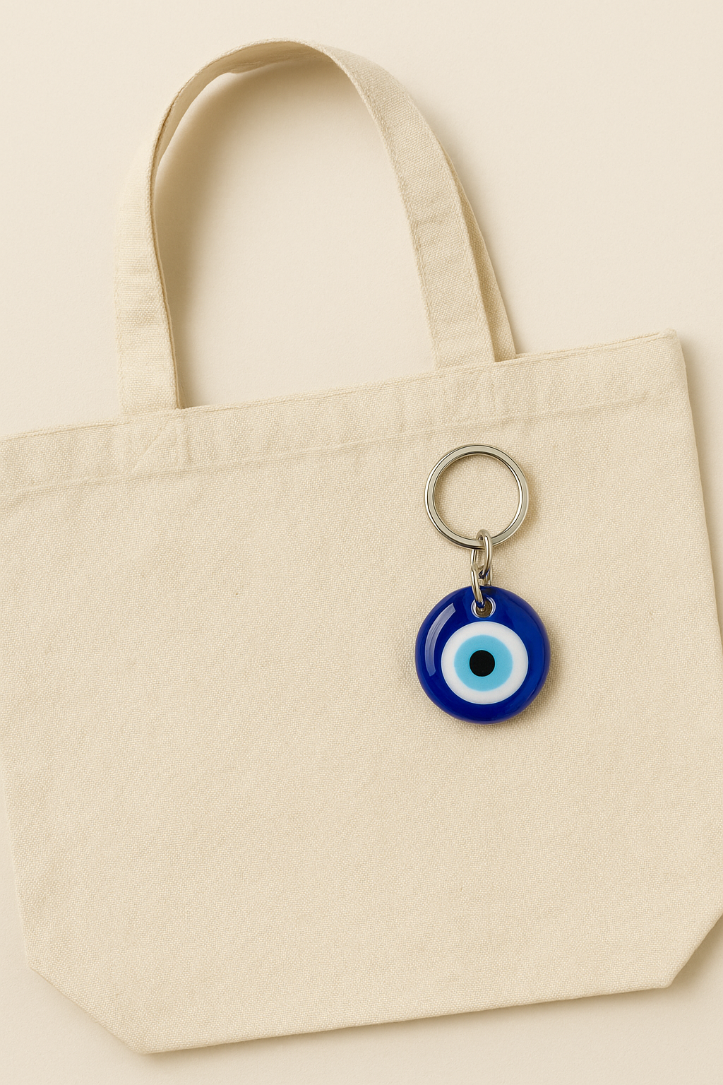 Beige tote bag with a blue evil eye keychain on a beige background