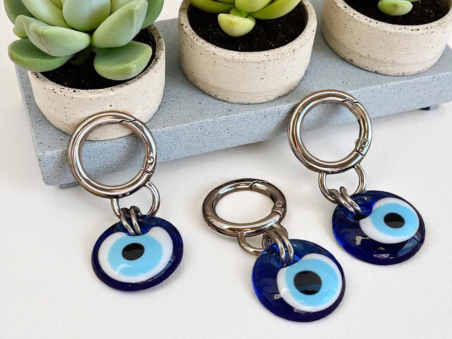Keychains with blue and white evil eye charms on a white surface with potted plants in the background.