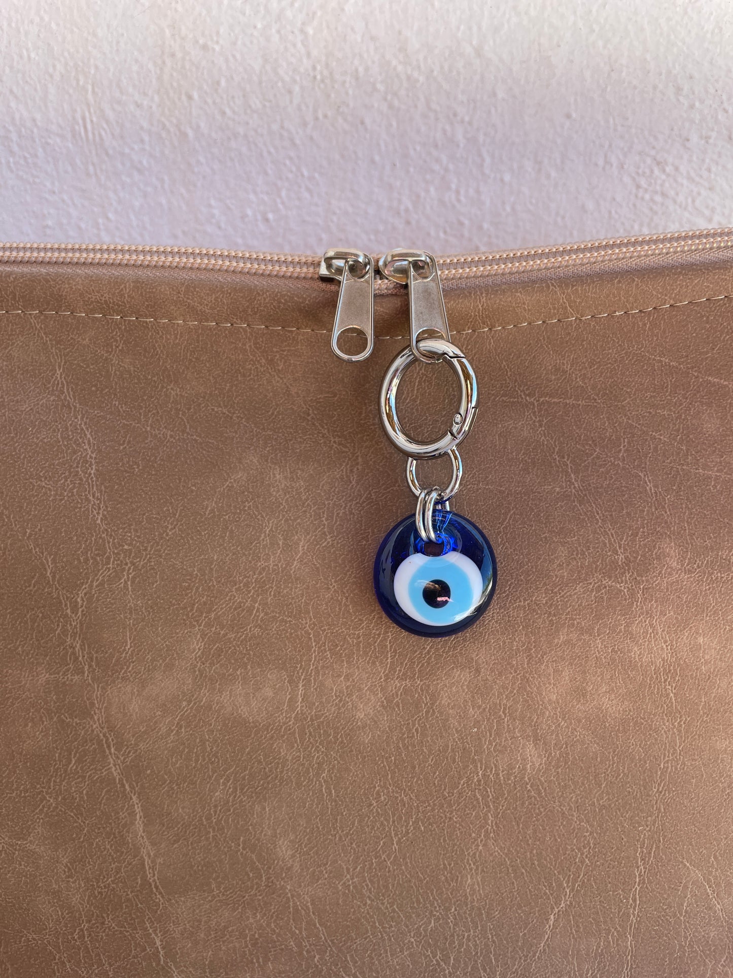 Close-up of a brown leather bag with an evil eye charm on a neutral background