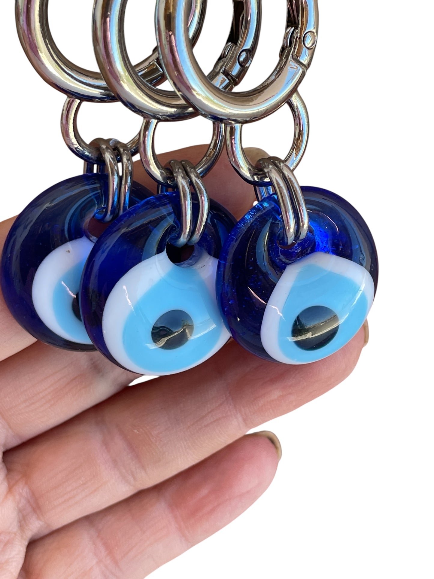 Blue evil eye keychains with silver rings held in a hand against a white background