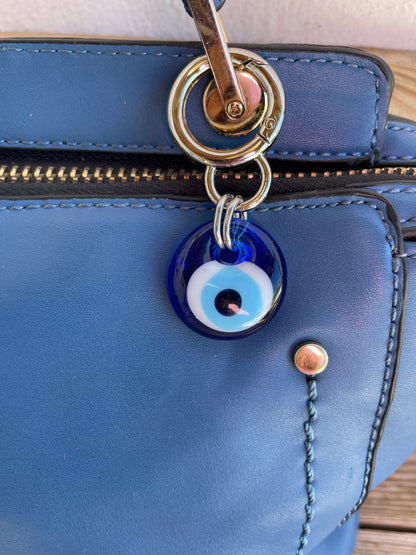 Blue leather bag with a blue evil eye charm attached to a gold ring.