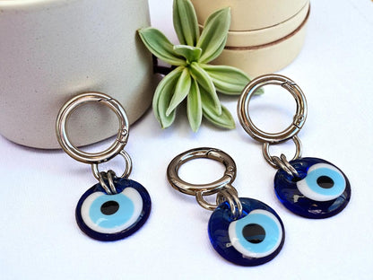 Three blue evil eye keychains on a white surface with a plant in the background.