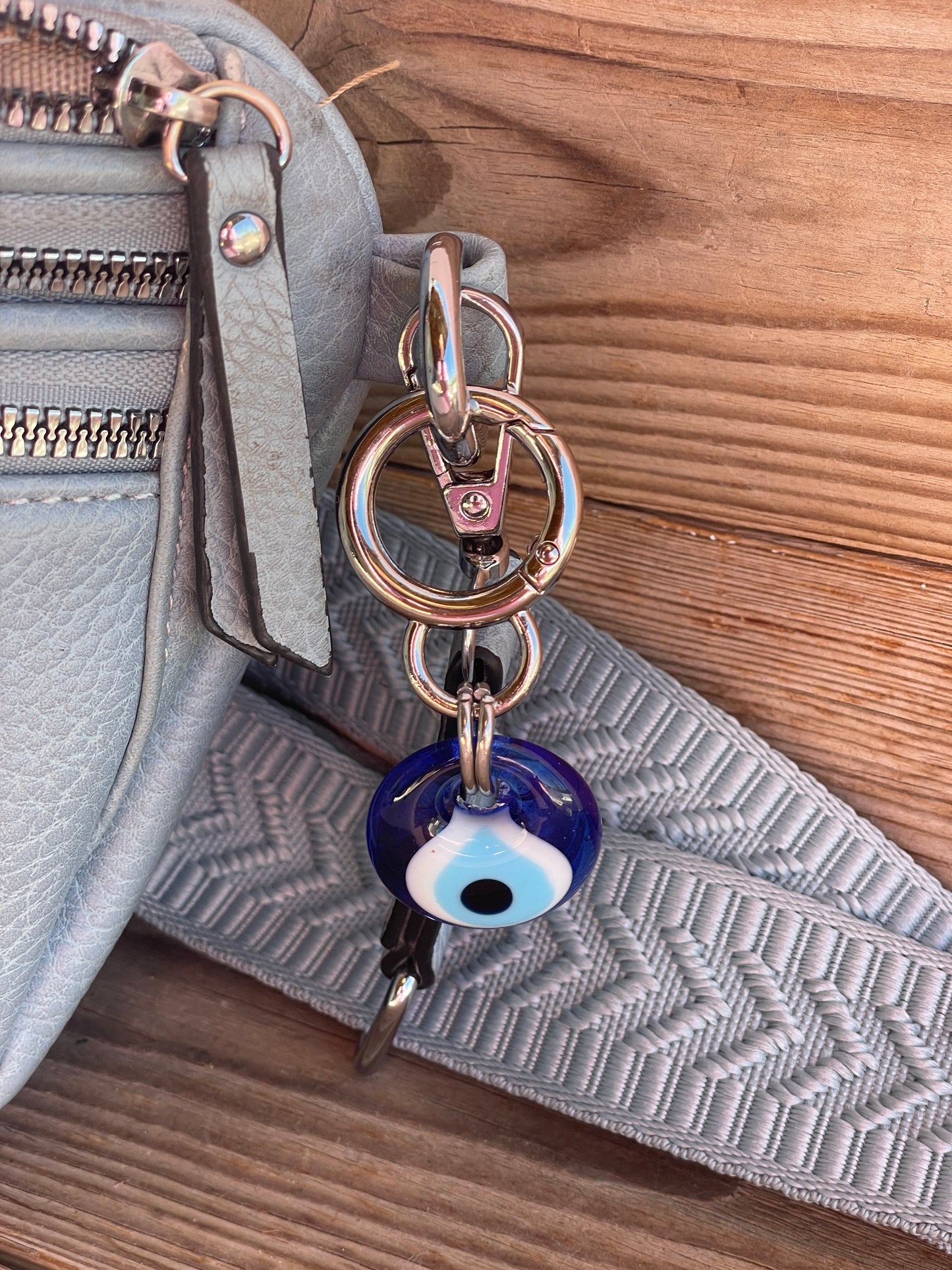 Close-up of a gray bag with a keychain featuring an evil eye charm on a wooden surface.