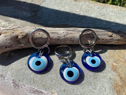 Three blue evil eye keychains on a stone surface with a piece of driftwood.