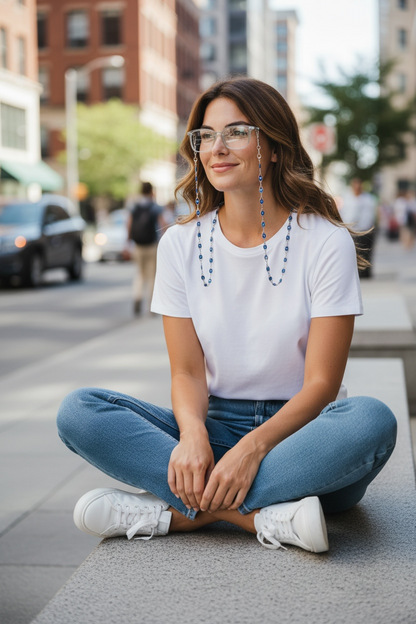 Woman sitting on a city street wearing a white t-shirt, blue jeans, and white sneakers.