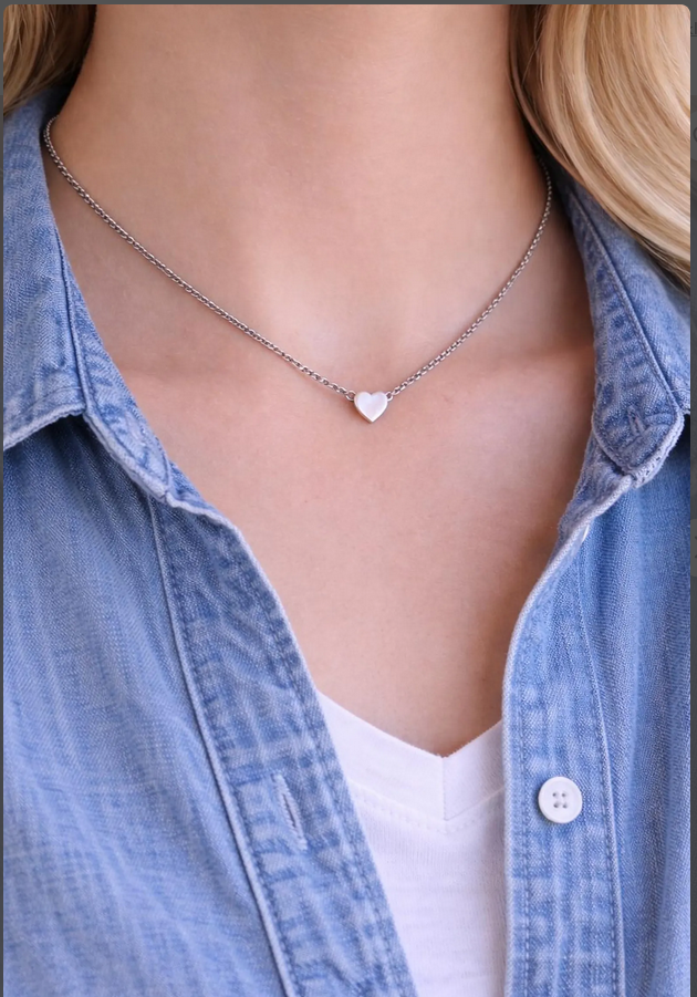 Necklace with a heart pendant worn by a person wearing a denim shirt.