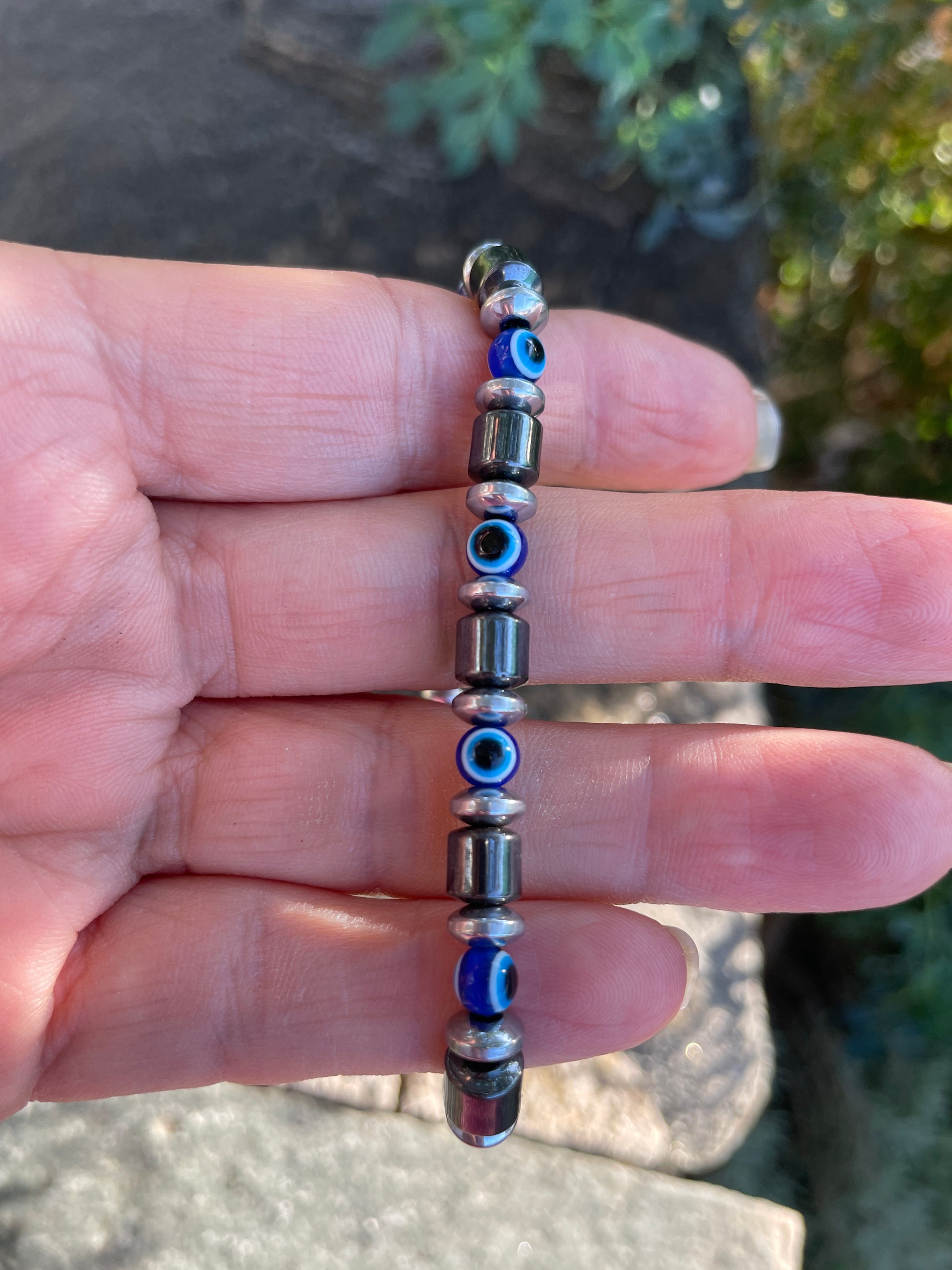 Hand holding a beaded bracelet with blue and silver beads against a natural background