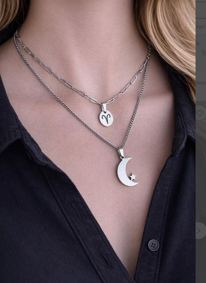 Two silver necklaces with heart and moon pendants on a person wearing a black shirt.