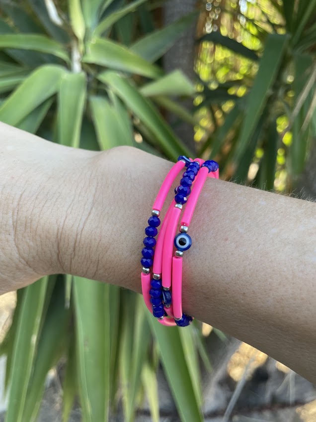 Pink and blue beaded bracelets on a wrist with a blurred green plant background