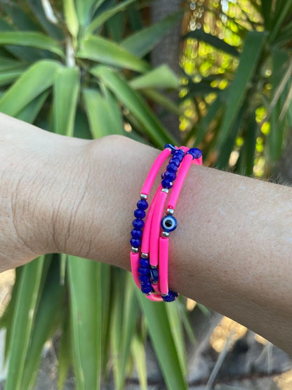 Pink and blue beaded bracelets on a wrist with a blurred green plant background