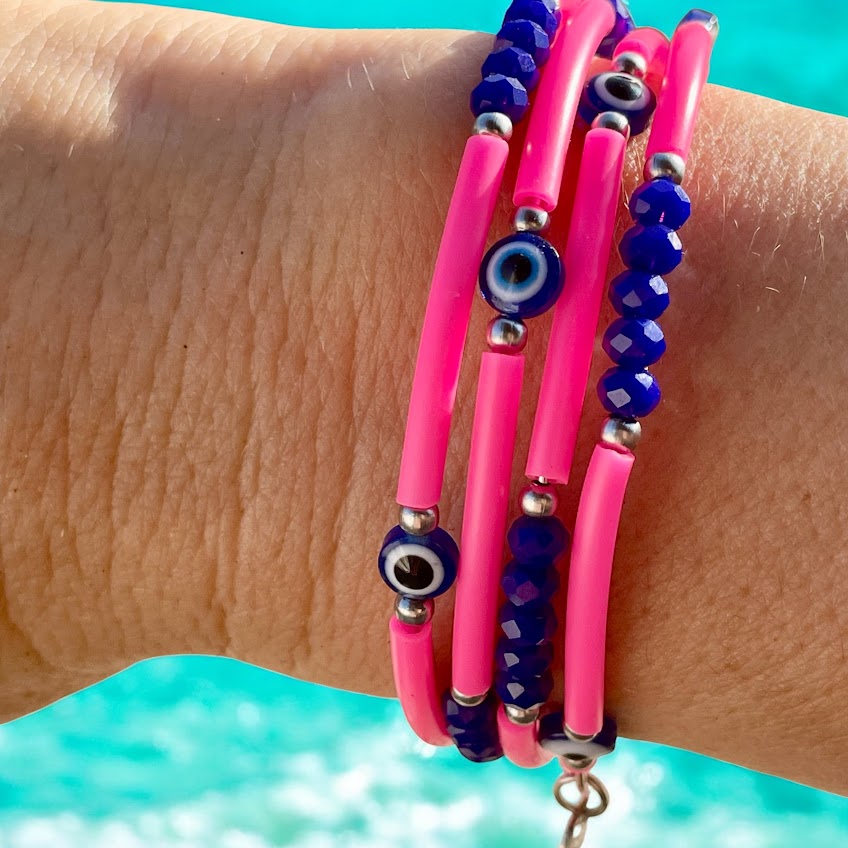 Close-up of a wrist wearing pink and blue beaded bracelets with a blurred blue background